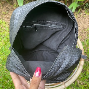 May include: Black leather backpack with a snakeskin pattern. The backpack is open and the inside is lined with black fabric. There is a zippered pocket on the inside of the flap.