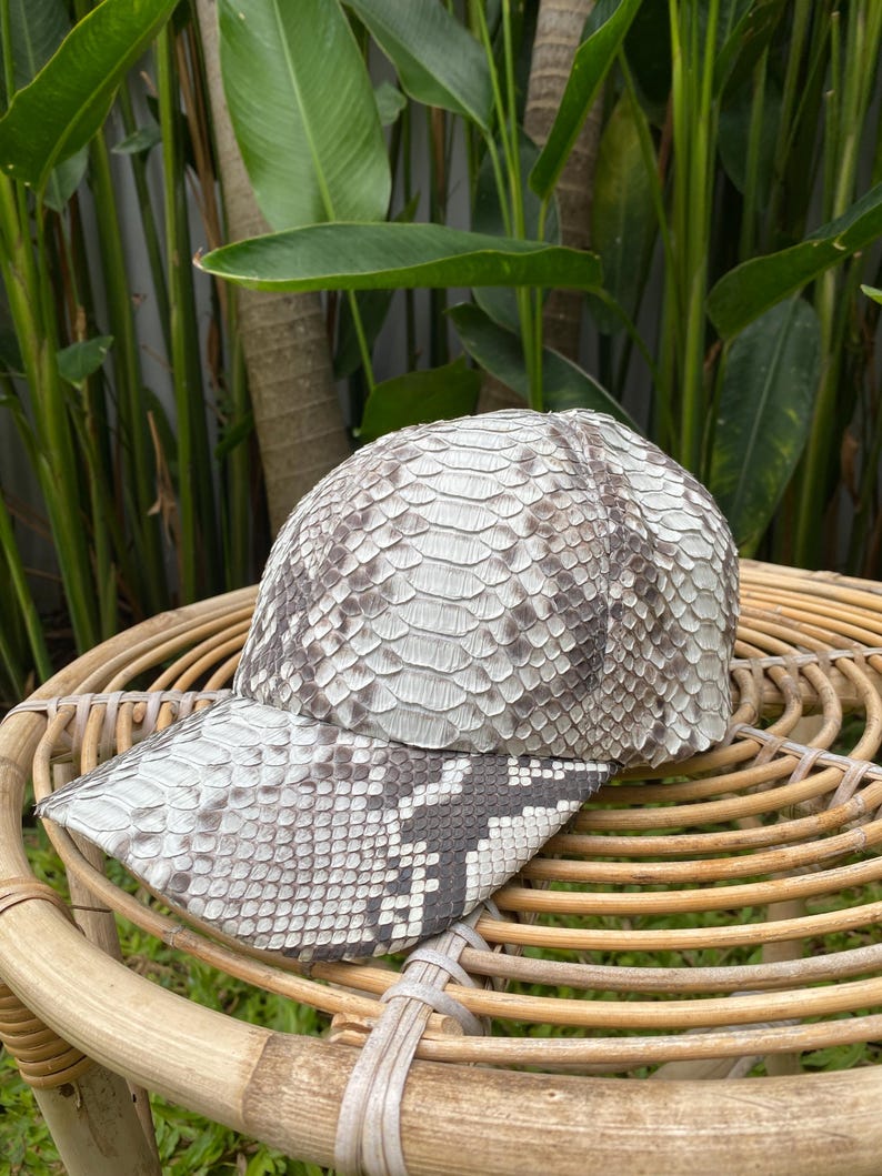 May include: A white and gray snakeskin baseball cap with a curved brim. The cap is made of real snakeskin and has a unique, textured pattern.