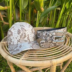 May include: A brown and white snakeskin baseball cap and belt set. The cap has a curved brim and the belt has a silver buckle.