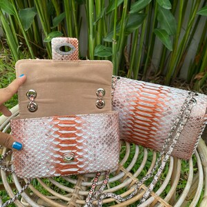 May include: Two small, pink and white snakeskin purses with silver chains. The purses have a flap closure and a silver chain strap.