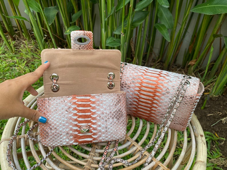 May include: Two small, pink and white snakeskin purses with silver chains. The purses have a flap closure and a silver chain strap.