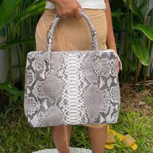 May include: A grey and white snakeskin tote bag with a top handle.