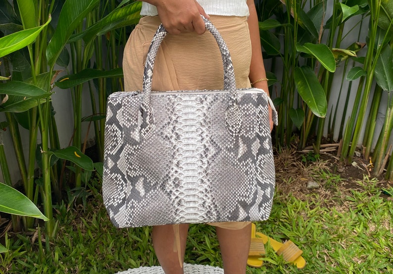 May include: A grey and white snakeskin tote bag with a top handle.