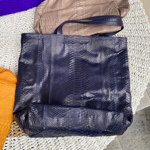 Puede incluir: Un bolso tote de piel de serpiente azul marino con un asa de cuero azul oscuro. El bolso est&aacute; hecho de un material texturizado y tiene un interior espacioso.