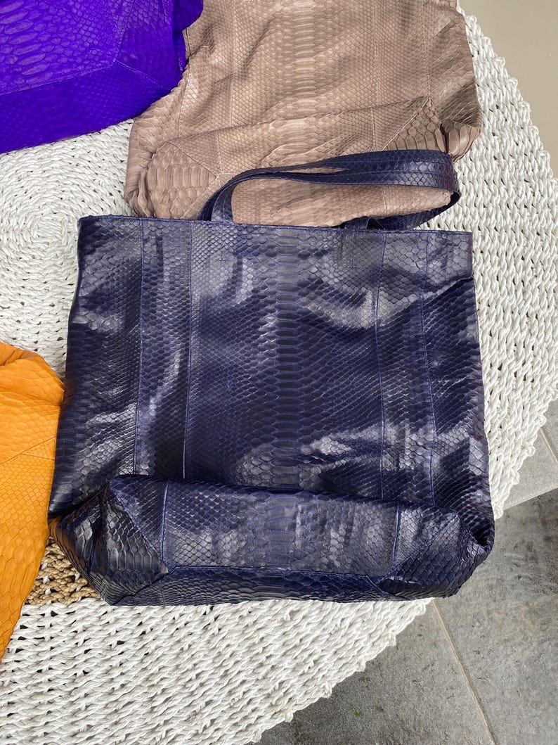 Puede incluir: Un bolso tote de piel de serpiente azul marino con un asa de cuero azul oscuro. El bolso est&aacute; hecho de un material texturizado y tiene un interior espacioso.