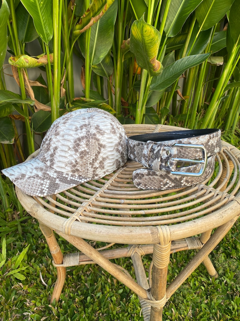 May include: A brown and white snake skin patterned baseball cap and belt set. The cap has a curved brim and the belt has a silver buckle.