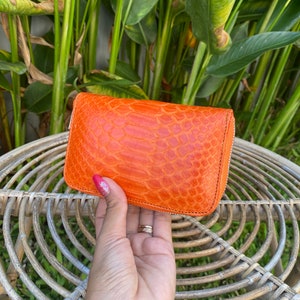 May include: A bright orange leather wallet with a textured, snake-skin pattern. The wallet has a zipper closure.