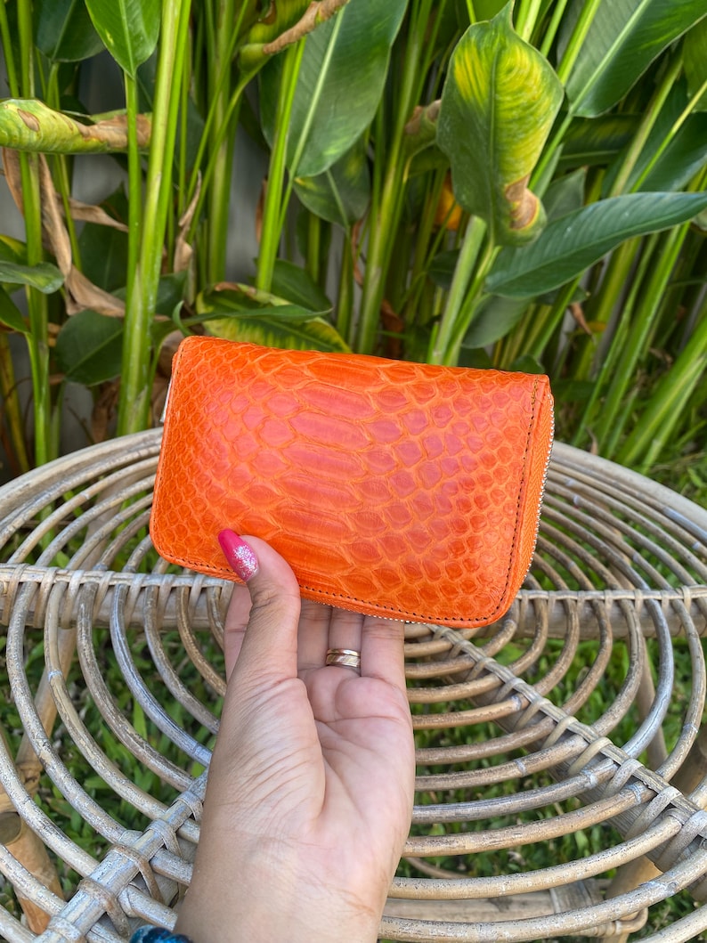 May include: A bright orange leather wallet with a textured, snake-skin pattern. The wallet has a zipper closure.