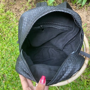 May include: Black leather backpack with a snakeskin pattern. The backpack is open and the inside is lined with black fabric. There is a zipped pocket on the inside of the backpack.