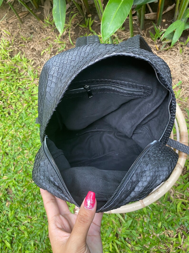 May include: Black leather backpack with a snakeskin pattern. The backpack is open and the inside is lined with black fabric. There is a zipped pocket on the inside of the backpack.