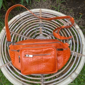 May include: Orange snakeskin leather fanny pack with a silver chain strap and two zipped compartments.