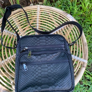 May include: A black leather crossbody bag with a snakeskin pattern. The bag has multiple zippered compartments and a long adjustable strap.