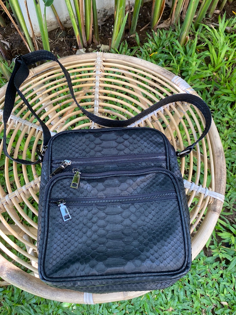 May include: A black leather crossbody bag with a snakeskin pattern. The bag has multiple zippered compartments and a long adjustable strap.