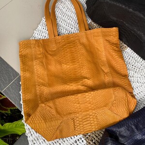 Puede incluir: Un bolso tote grande de piel de serpiente amarillo con dos asas. El bolso est&aacute; hecho de un material texturizado y tiene una forma ligeramente redondeada.