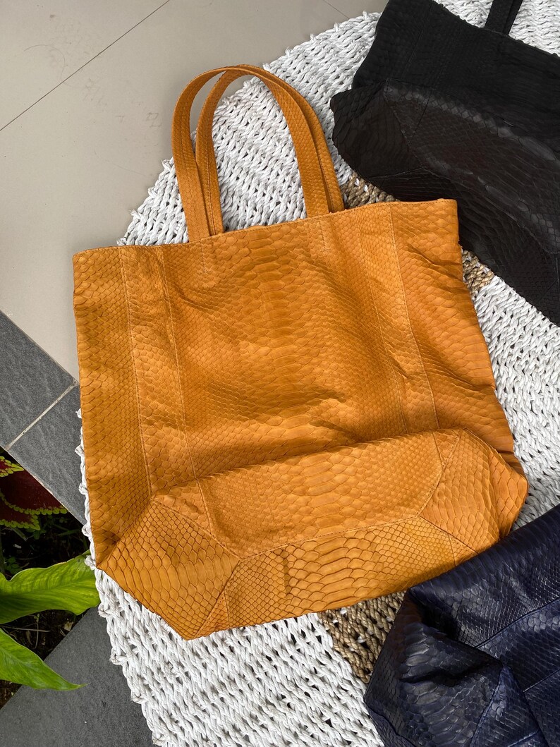 Puede incluir: Un bolso tote grande de piel de serpiente amarillo con dos asas. El bolso est&aacute; hecho de un material texturizado y tiene una forma ligeramente redondeada.