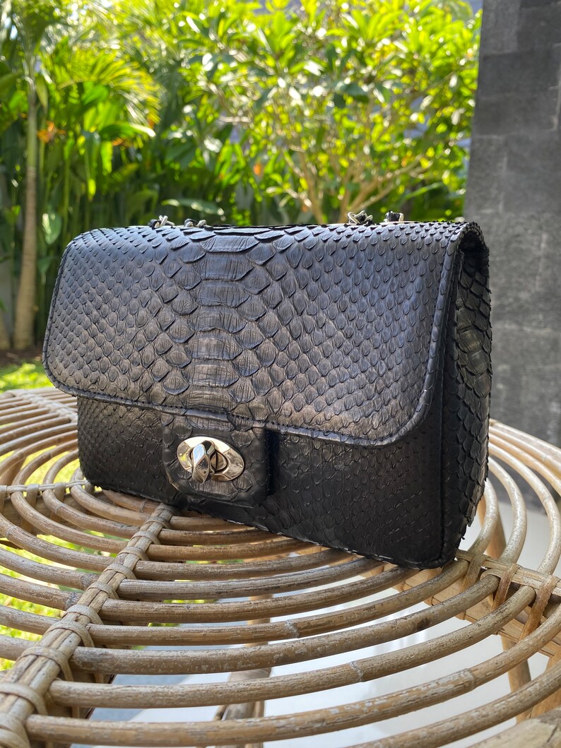 以下が含まれることがあります： シルバーのチェーンストラップとシルバーの留め金が付いた、黒いヘビ革のショルダーバッグです。