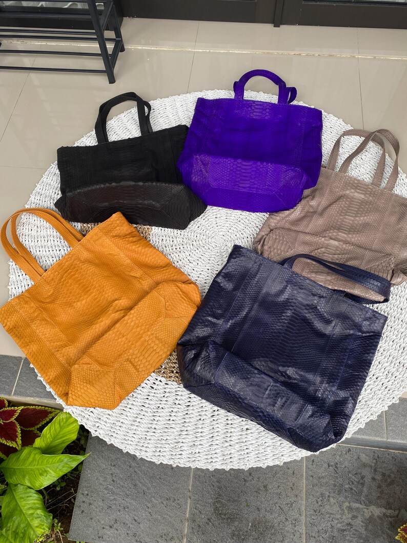 Puede incluir: Cinco bolsos de mano diferentes hechos de piel de serpiente. Los bolsos son de varios colores, incluyendo negro, morado, marr&oacute;n, naranja y azul.