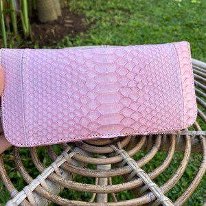 Peut inclure: Un portefeuille en cuir de serpent rose avec une fermeture &eacute;clair.