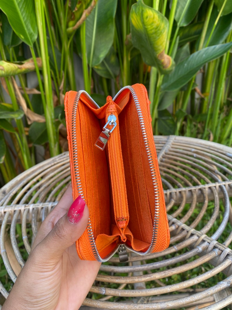 May include: Orange leather zippered wallet with a silver zipper. The wallet is open and the inside is lined with a soft orange fabric.