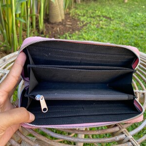 Peut inclure: Un portefeuille zipp&eacute; rose avec un int&eacute;rieur noir et plusieurs emplacements pour cartes. Le portefeuille est ouvert et la fermeture &eacute;clair est visible.