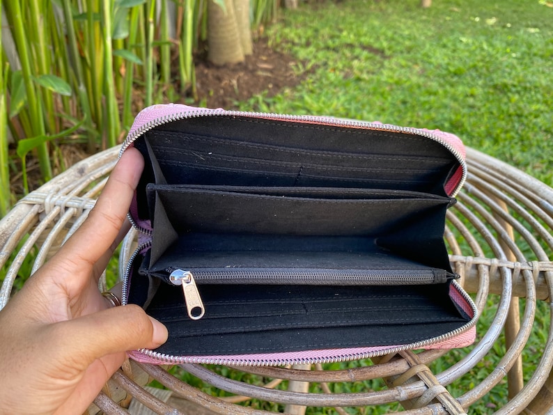 Peut inclure: Un portefeuille zipp&eacute; rose avec un int&eacute;rieur noir et plusieurs emplacements pour cartes. Le portefeuille est ouvert et la fermeture &eacute;clair est visible.