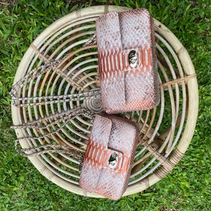 May include: Two small, brown and white snakeskin purses with silver chains and clasps. The purses are sitting on a woven wicker chair.