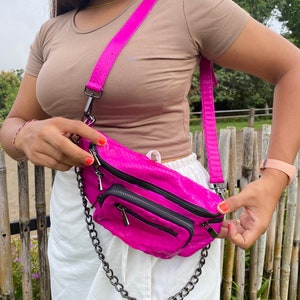 Może przedstawiać: Różowa nerka o fakturze skóry węża, ze srebrnym łańcuszkiem i czarnymi zamkami.