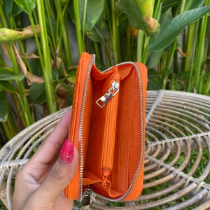 May include: Orange leather zippered wallet with a silver zipper. The wallet is open and the inside is lined with orange fabric.