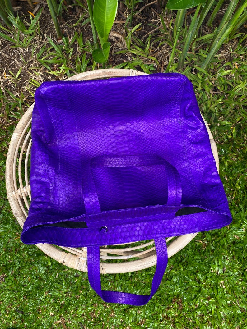 Puede incluir: Un bolso tote de cuero morado con estampado de piel de serpiente. El bolso tiene dos asas superiores y una sola correa.