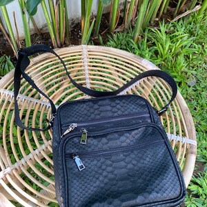 May include: A black leather crossbody bag with a snakeskin pattern. The bag has two zippered compartments and a silver zipper pull.