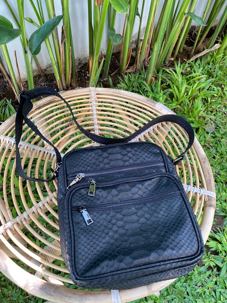 May include: A black leather crossbody bag with a snakeskin pattern. The bag has two zippered compartments and a silver zipper pull.