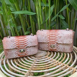 May include: Two small, light pink snakeskin purses with silver hardware. The purses are sitting on a woven wicker stool.