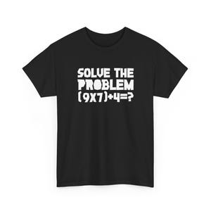 Puede incluir: Camiseta negra con el texto blanco "SOLVE THE PROBLEM (9X7)+4=?". La camiseta de cuello redondo tiene mangas cortas y está hecha de una tela suave. El texto está en negrita y centrado en la parte delantera.