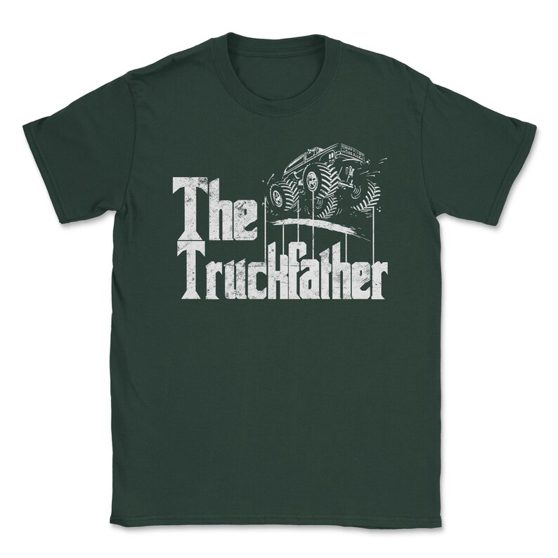 Op de afbeelding: Donkergroen t-shirt met een witte afbeelding van een monstertruck en de tekst "The Truckfather". Het ontwerp heeft een verweerde lettertype en een gedetailleerde illustratie van de truck.
