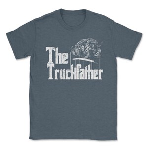 Op de afbeelding: Blauw t-shirt met de witte tekst "The Truckfather" en een afbeelding van een monstertruck. Het ontwerp heeft een vintage uitstraling.