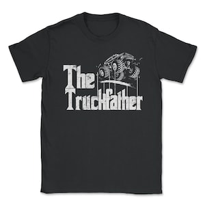 Op de afbeelding: Zwart t-shirt met een witte afbeelding van een monstertruck en de tekst "The Truckfather". Het ontwerp toont een gestileerde monstertruck met grote banden en de titel in een vet, verweerd lettertype. Een uniek kledingstuk.