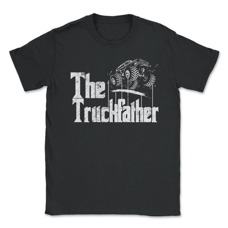 Op de afbeelding: Zwart t-shirt met een witte afbeelding van een monstertruck en de tekst "The Truckfather". Het ontwerp toont een gestileerde monstertruck met grote banden en de titel in een vet, verweerd lettertype. Een uniek kledingstuk.