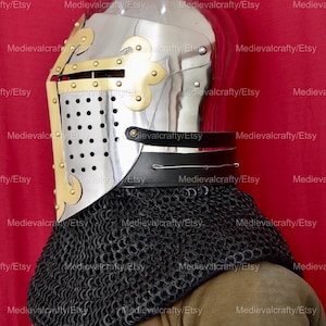 May include: A silver helmet with a brass visor and a black leather strap. The helmet is decorated with brass rivets and a brass fleur-de-lis design. The helmet is worn over a black chainmail coif.