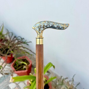 May include: A wooden walking stick with a brass handle featuring a white and gold floral design.