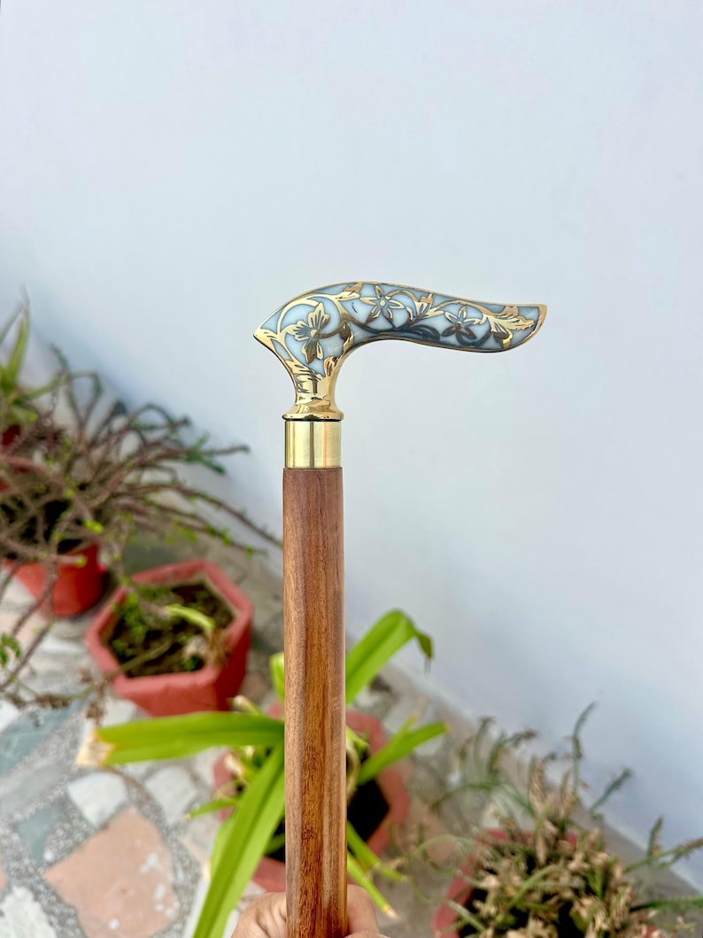 May include: A wooden walking stick with a brass handle featuring a white and gold floral design.