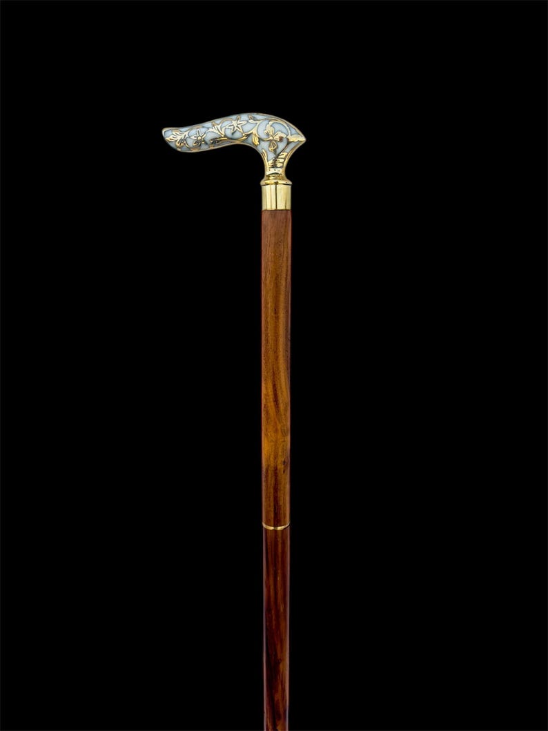 May include: A wooden walking stick with a decorative, white and gold handle. The handle has a floral design.