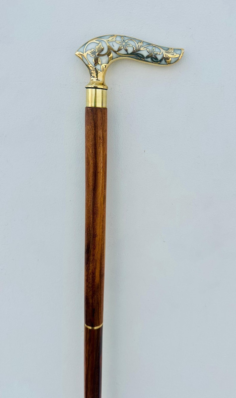 May include: A wooden walking stick with a brass handle featuring a white and gold floral design.