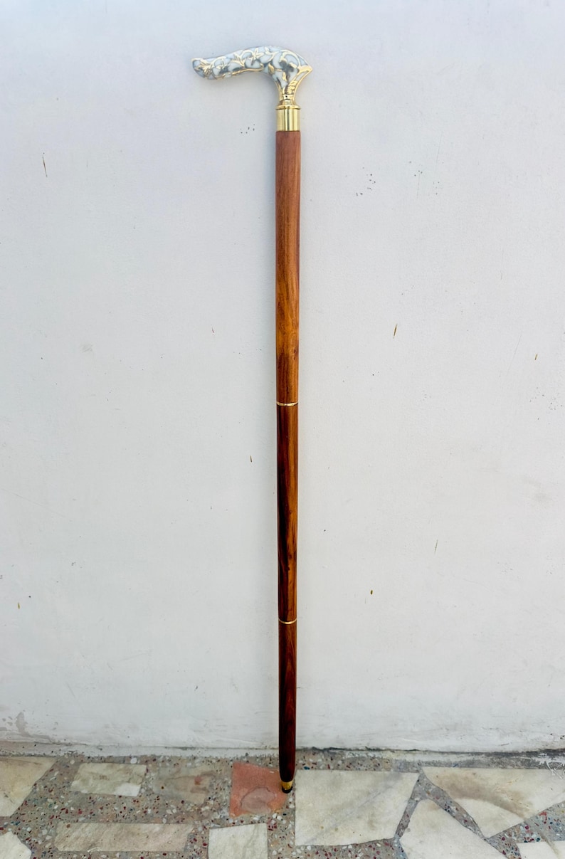 May include: A wooden walking stick with a decorative brass handle. The handle is shaped like a curved horn and has a silver finish.