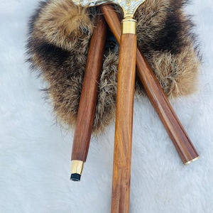 May include: Three wooden walking sticks with ornate metal handles. The handles are decorated with a floral design and have a gold finish. The sticks are resting on a white fur surface.