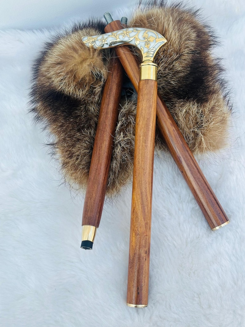 May include: Three wooden walking sticks with ornate metal handles. The handles are decorated with a floral design and have a gold finish. The sticks are resting on a white fur surface.