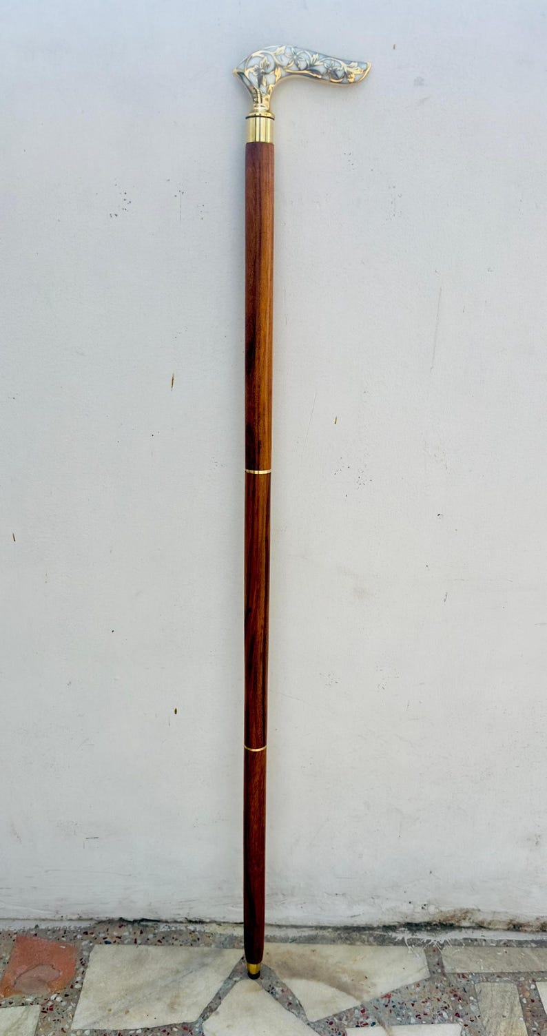 May include: A wooden walking stick with a brass handle featuring an ornate design. The handle is curved and has a gold finish.