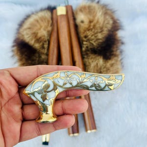 May include: A white and gold walking stick handle with a floral design. The handle is made of metal and has a smooth, polished finish.