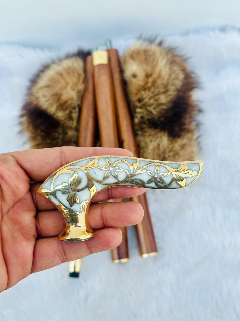 May include: A white and gold walking stick handle with a floral design. The handle is made of metal and has a smooth, polished finish.