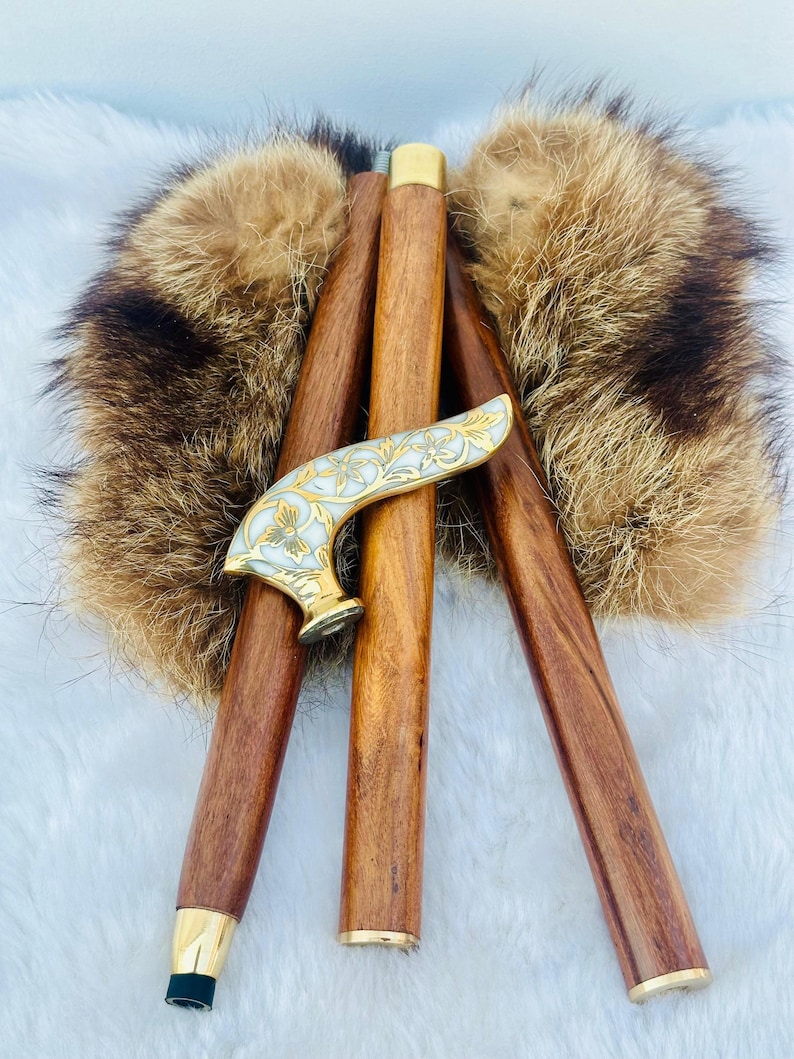 May include: Three wooden walking sticks with a decorative brass handle. The handle is inlaid with white mother of pearl and has a floral design. The sticks are resting on a brown fur surface.