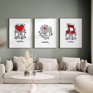 May include: Three framed black and white illustrations by Keith Haring. The illustrations depict two figures holding a red heart, a red flower, and a red musical note. Each illustration is framed in a white frame and has the artist's signature and name, "Keith Haring", at the bottom.